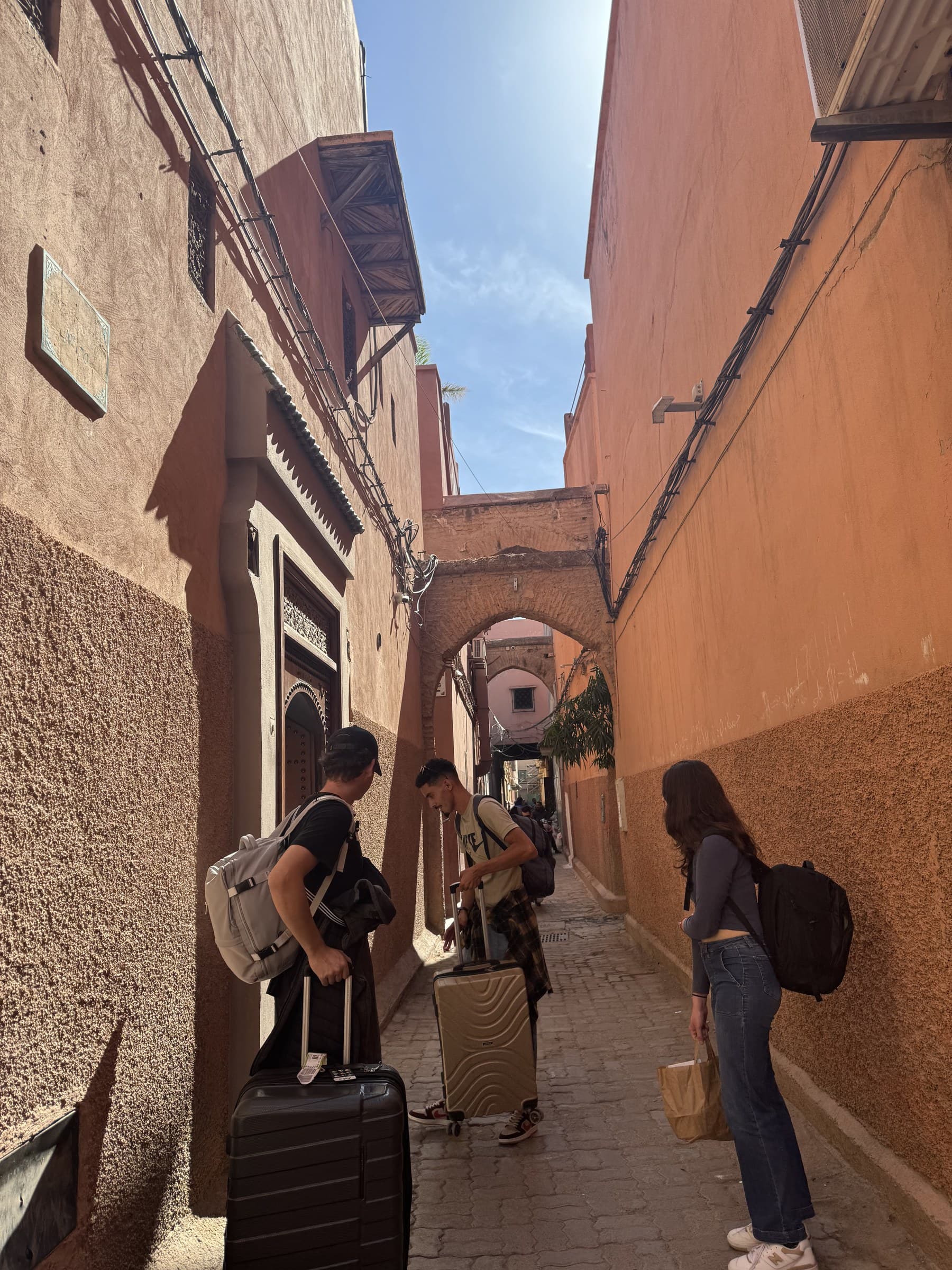Viajeros con maletas recorriendo un callejón de la medina roja de Marrakech bajo un arco tradicional