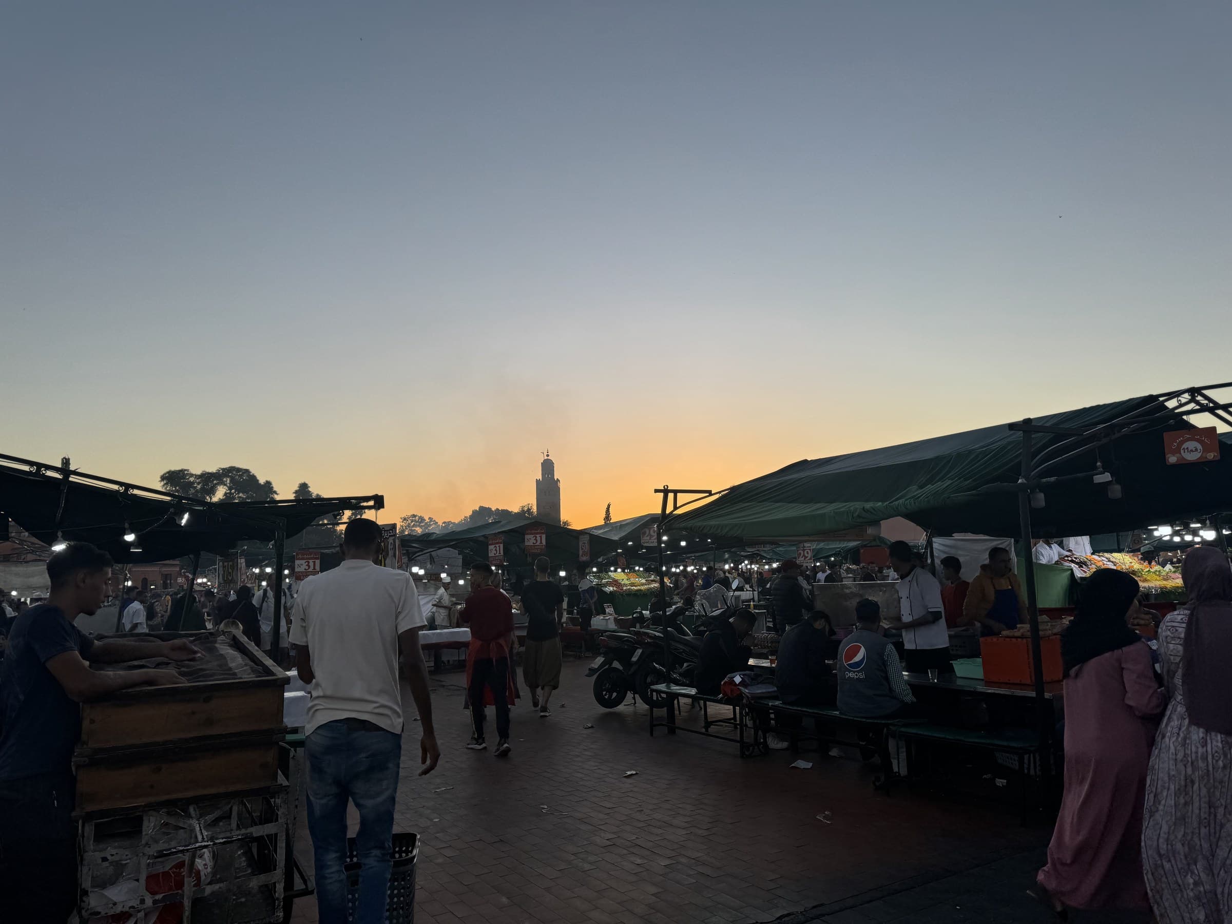 Atardecer en la plaza Jemaa el-Fna de Marrakech con puestos de comida y minarete de la Koutoubia al fondo