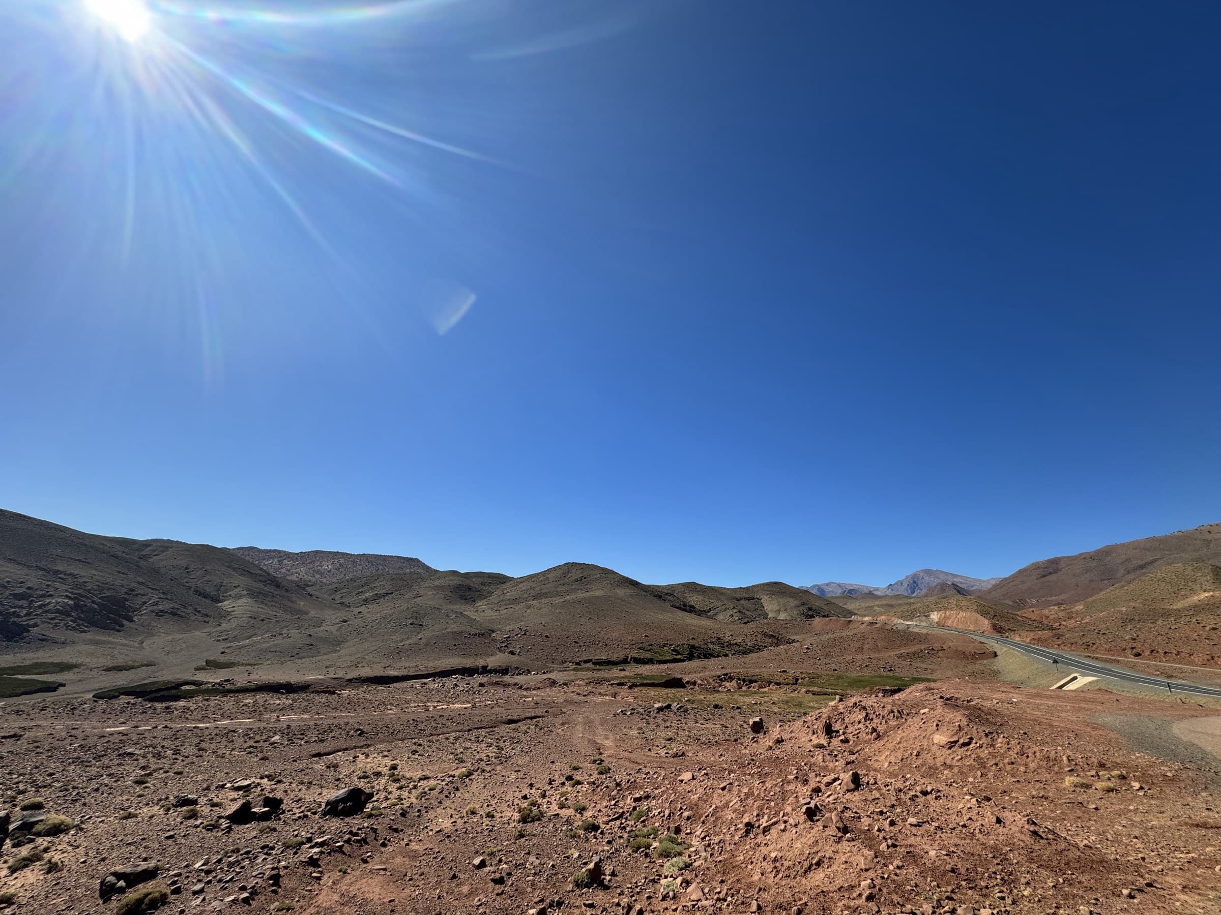 Paisaje árido del Alto Atlas marroquí con carretera sinuosa bajo cielo azul intenso y sol brillante