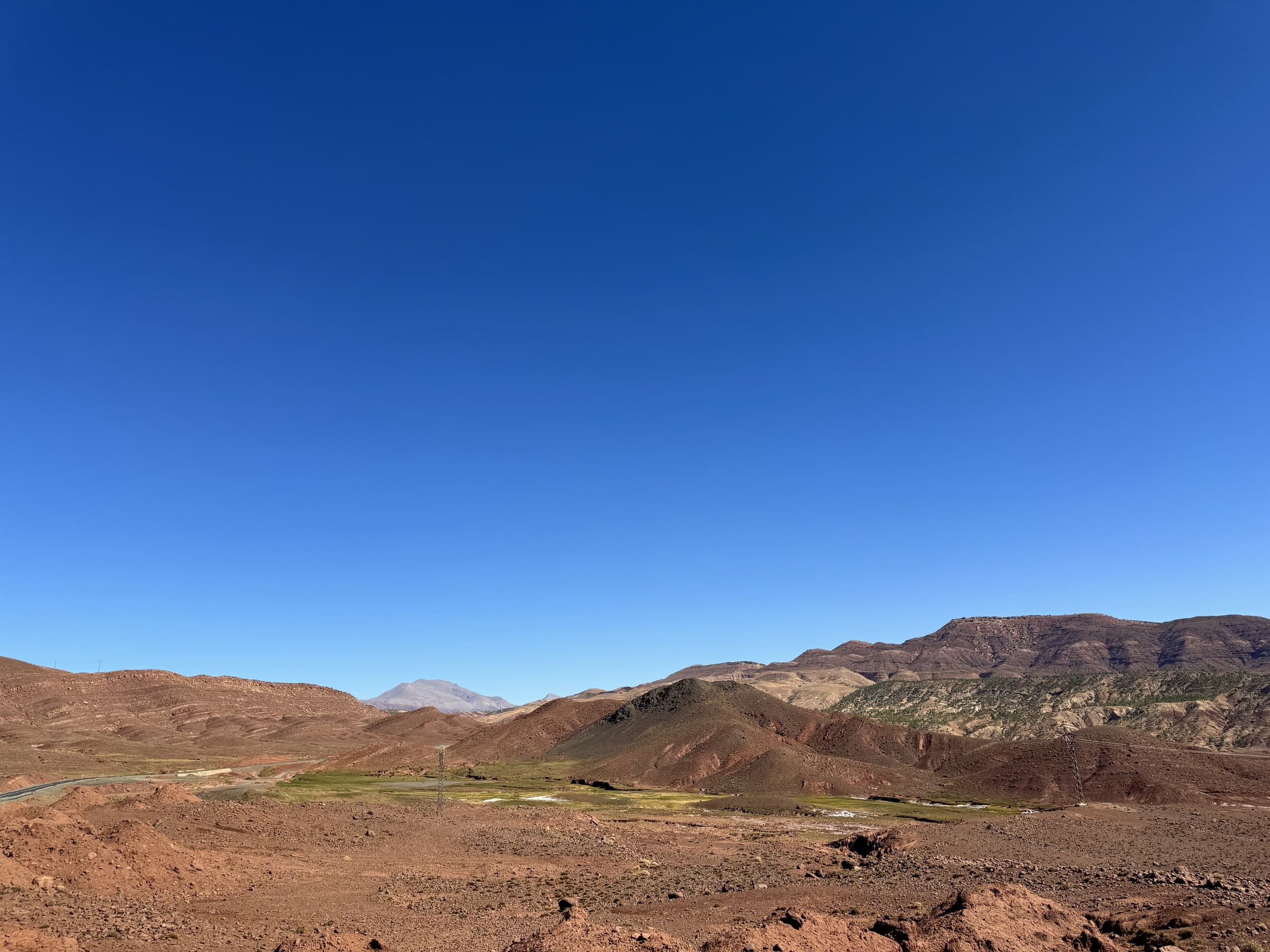 Valle árido del Alto Atlas marroquí con tierras rojizas, vegetación en el fondo y cielo azul intenso