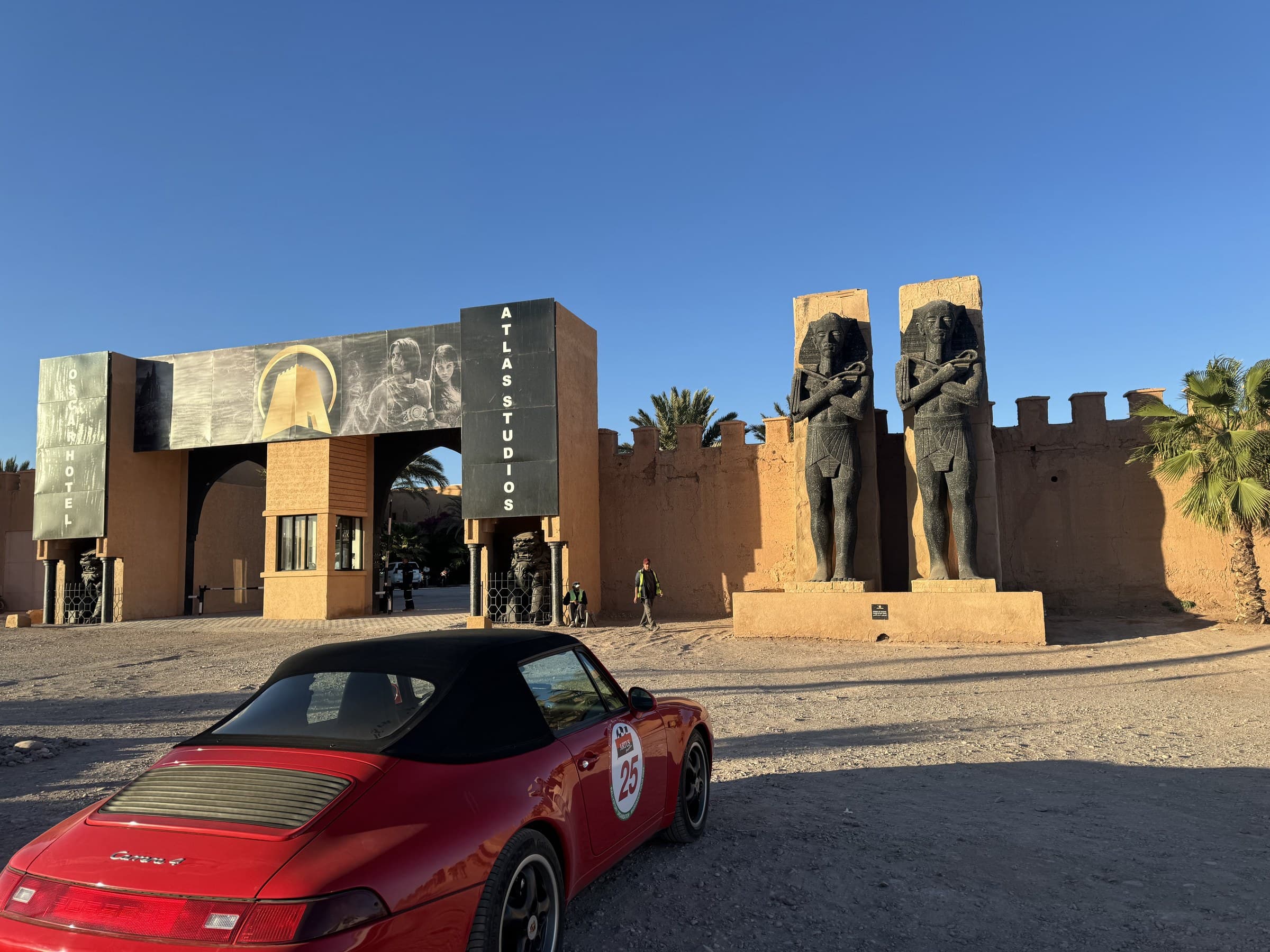 Entrada de Atlas Studios en Ouarzazate con estatuas faraónicas y Porsche rojo clásico aparcado