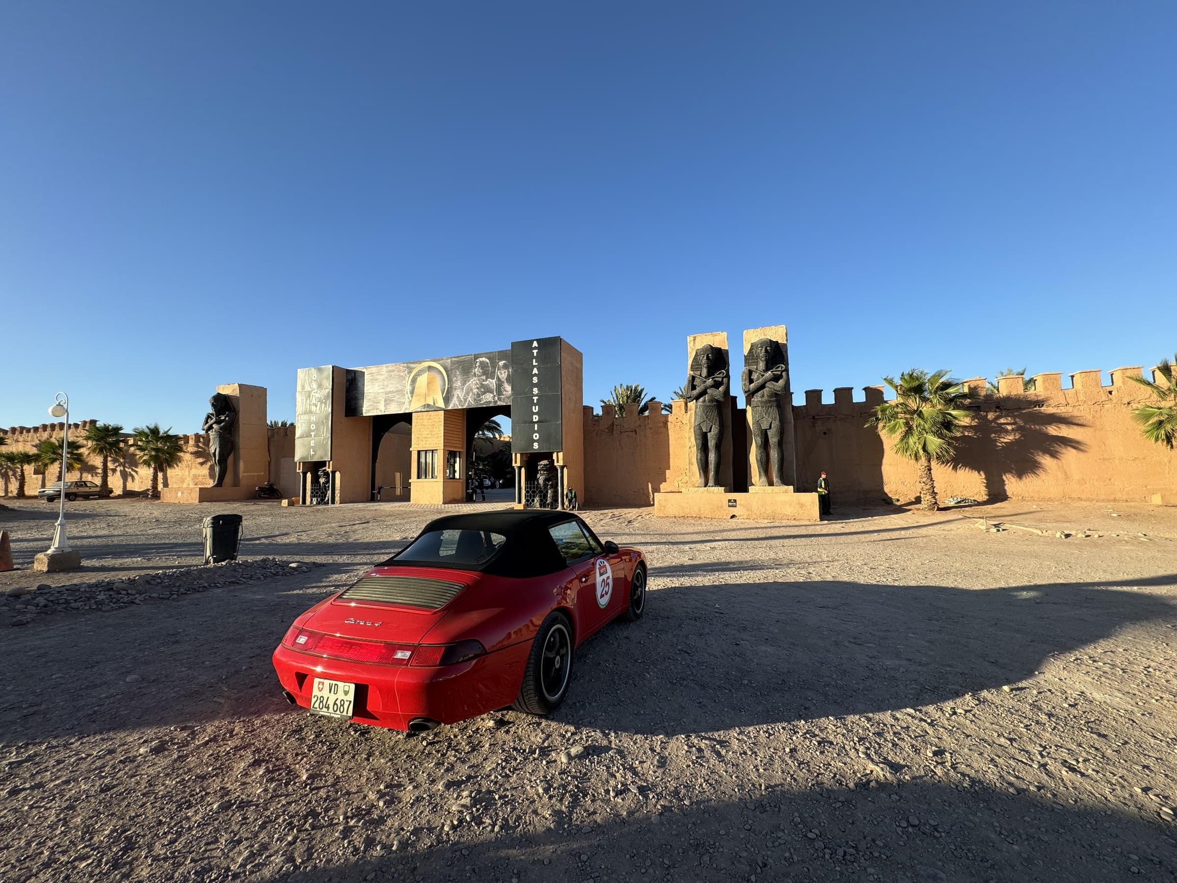 Entrada de Atlas Studios en Ouarzazate con estatuas faraónicas y un deportivo rojo aparcado, cielo azul despejado