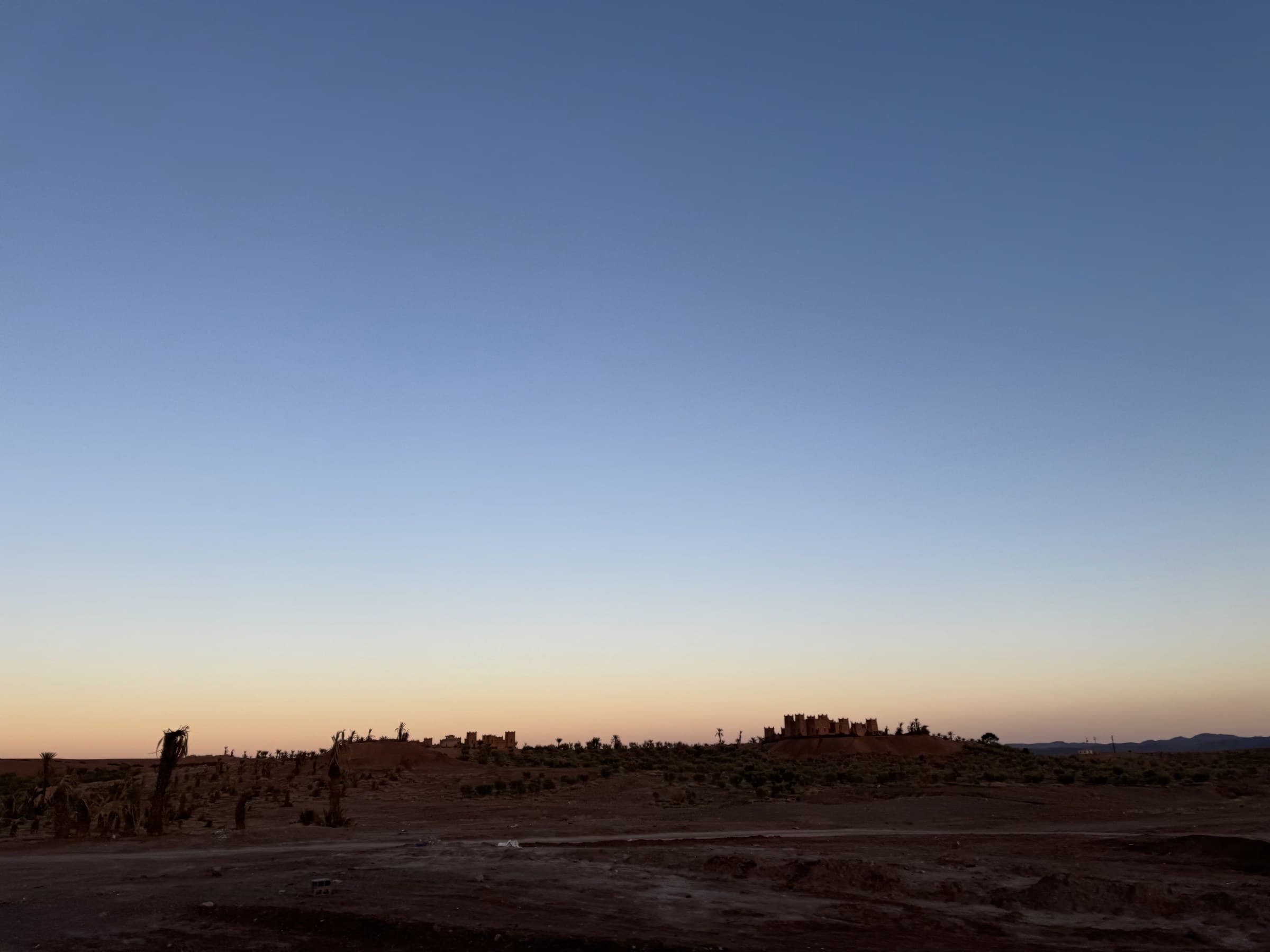 Silueta de kasbah de barro al atardecer en el sur de Marruecos con cielo degradado azul y naranja