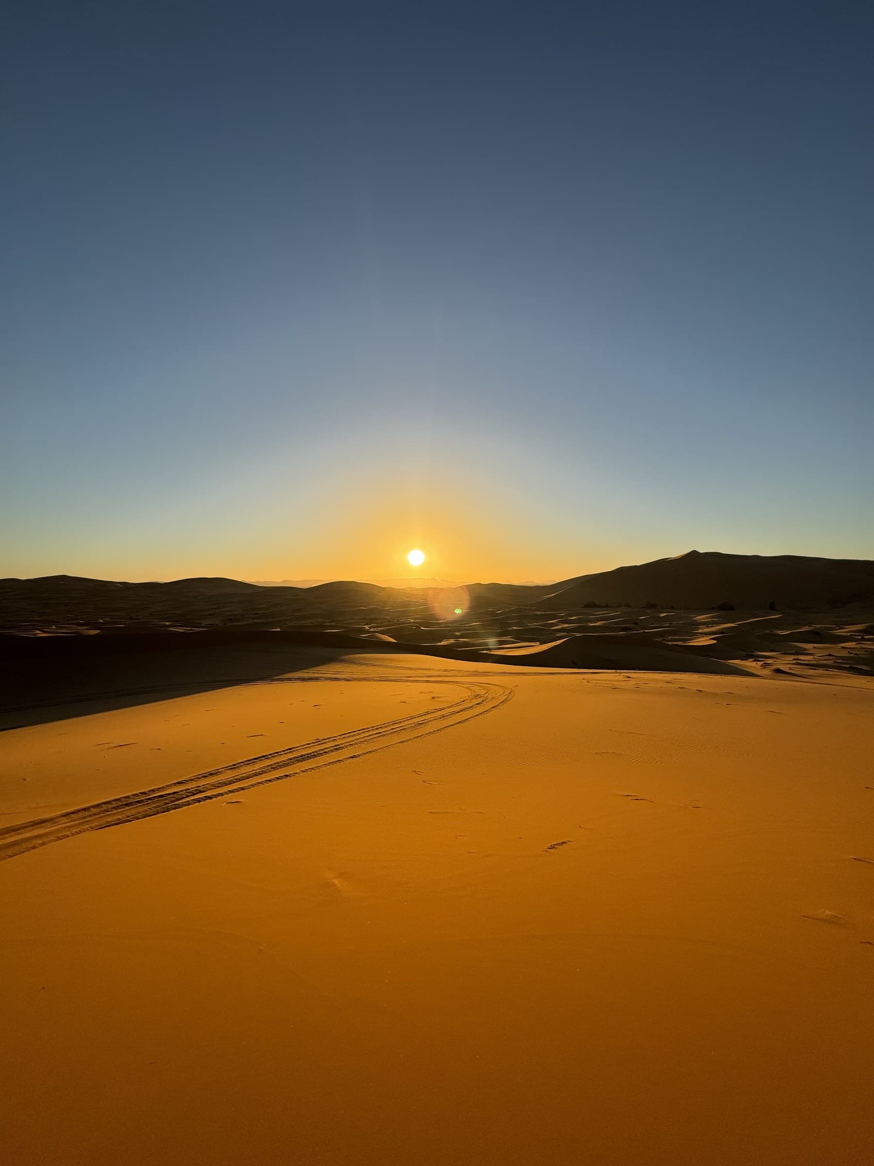Amanecer dorado sobre las dunas de Erg Chebbi en Merzouga, con huellas de 4x4 en la arena del Sahara