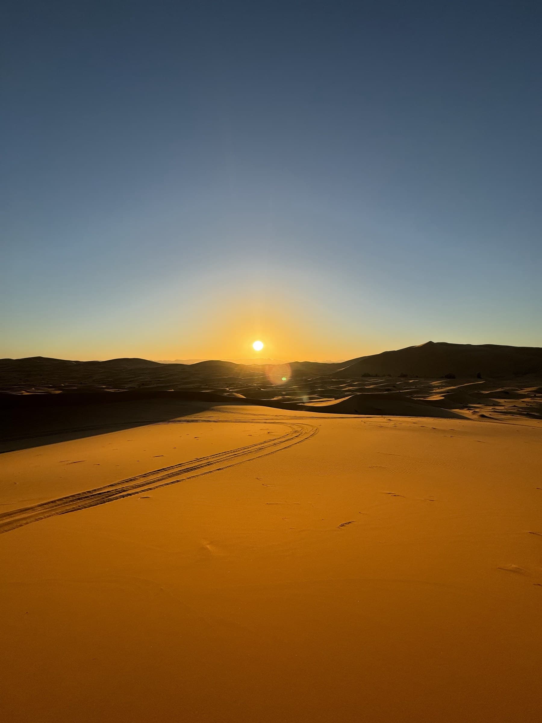 Amanecer dorado sobre las dunas de Erg Chebbi en Merzouga, Sahara marroquí, con huellas de 4x4 en la arena