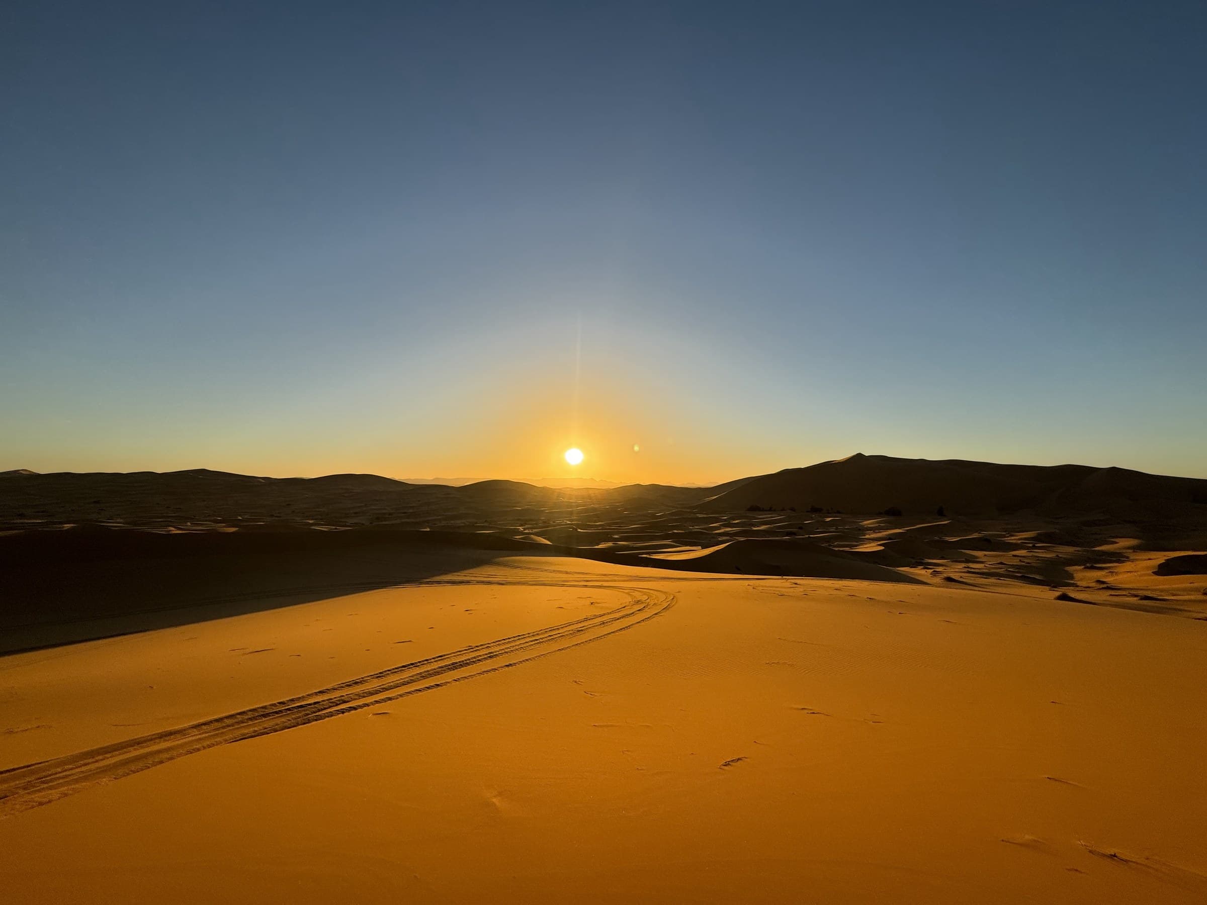 Amanecer dorado sobre las dunas del desierto de Merzouga con huellas de 4x4 en la arena del Erg Chebbi