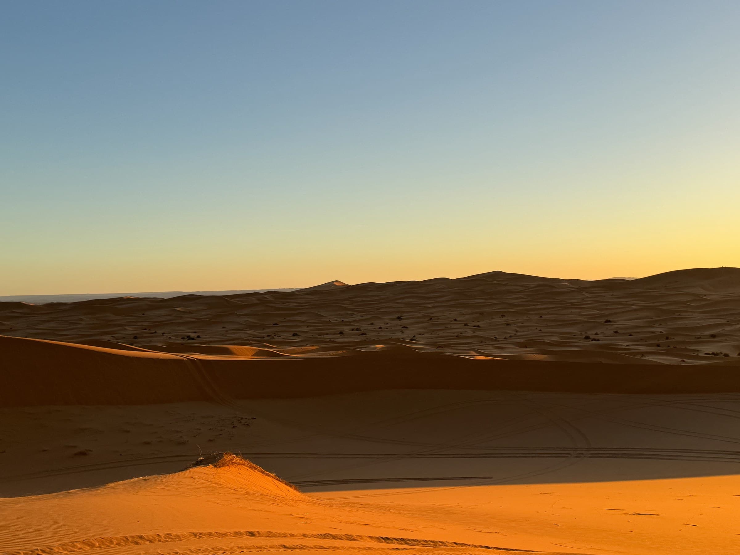 Dunas doradas del Erg Chebbi en Merzouga al atardecer con cielo degradado azul y naranja, Sahara marroquí