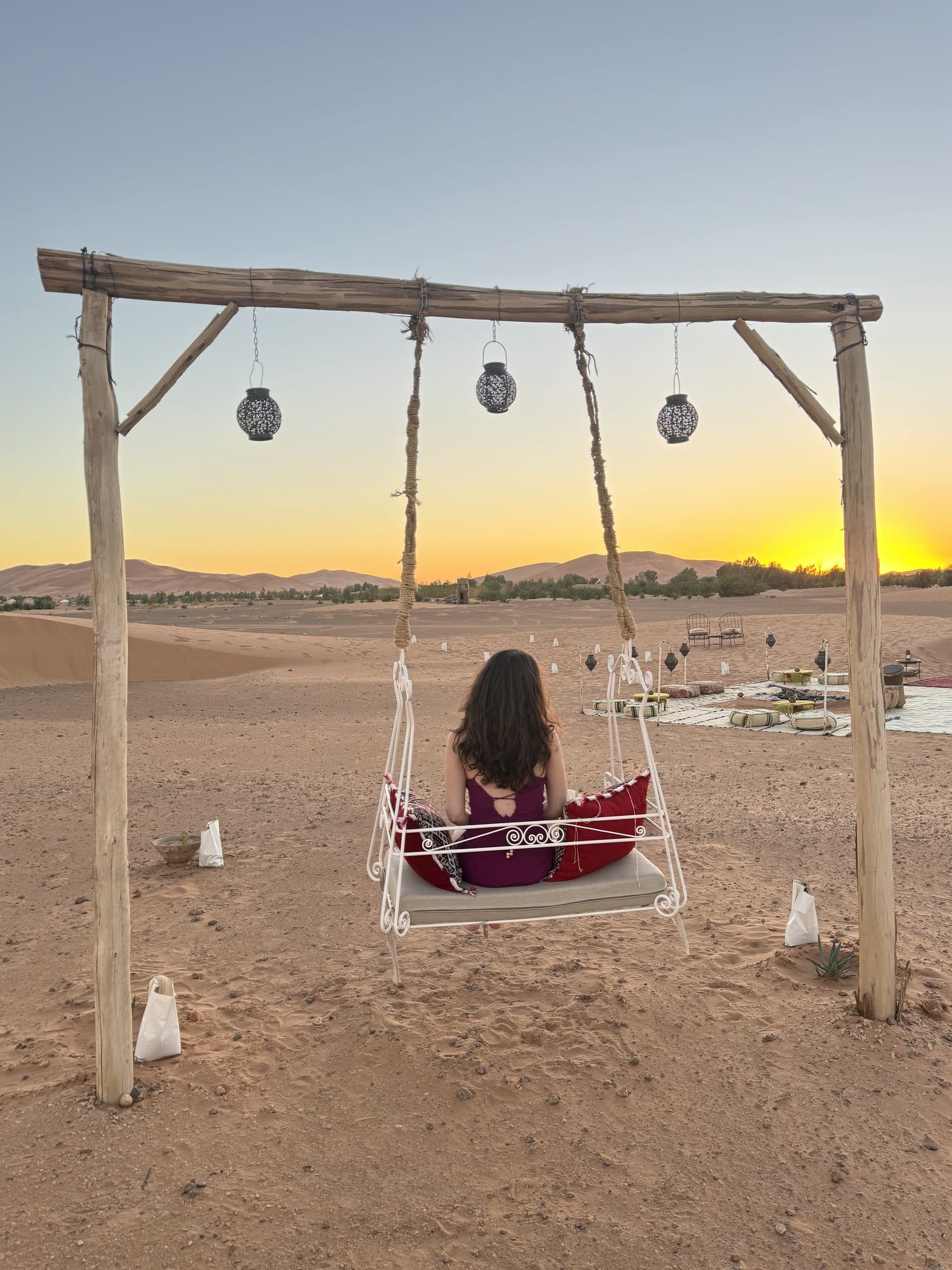 Mujer en columpio contemplando el atardecer dorado sobre las dunas del desierto de Merzouga, Sahara marroquí
