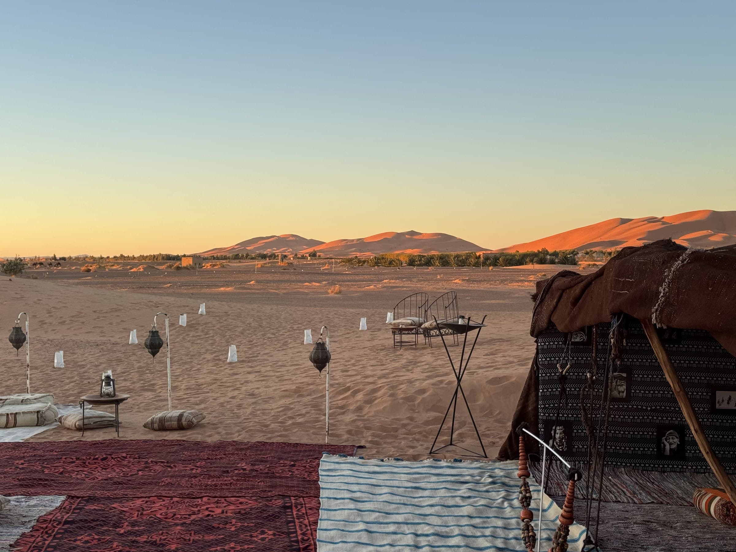 Campamento bereber en el desierto de Merzouga al atardecer con dunas del Erg Chebbi al fondo y linternas tradicionales