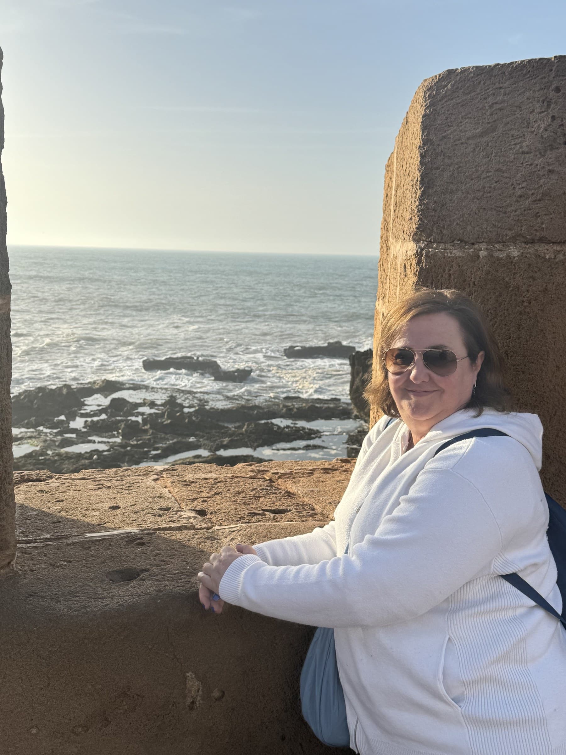 Viajera apoyada en las murallas de piedra de Essaouira con el océano Atlántico al fondo