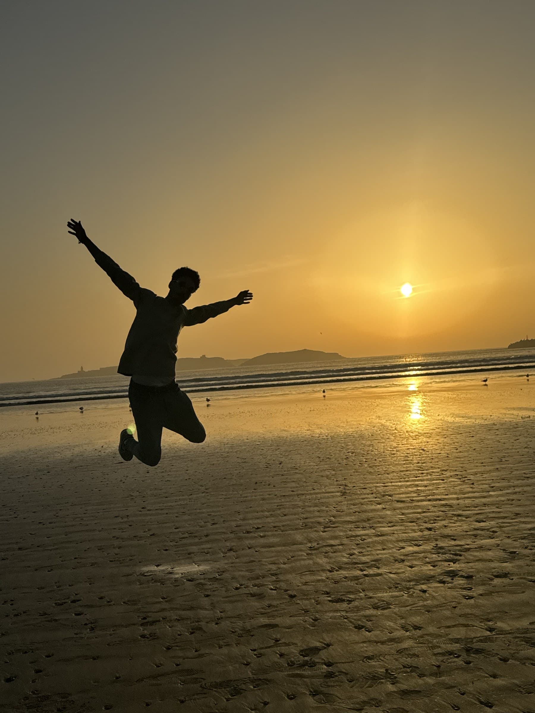 Silueta de viajero saltando en la playa de Essaouira al atardecer con el sol dorado sobre el Atlántico