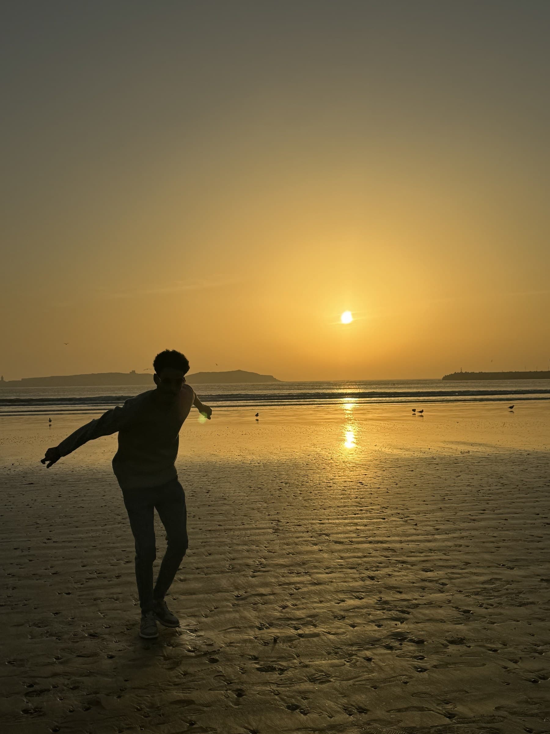 Silueta de persona bailando en la playa de Essaouira al atardecer con el sol dorado sobre el Atlántico