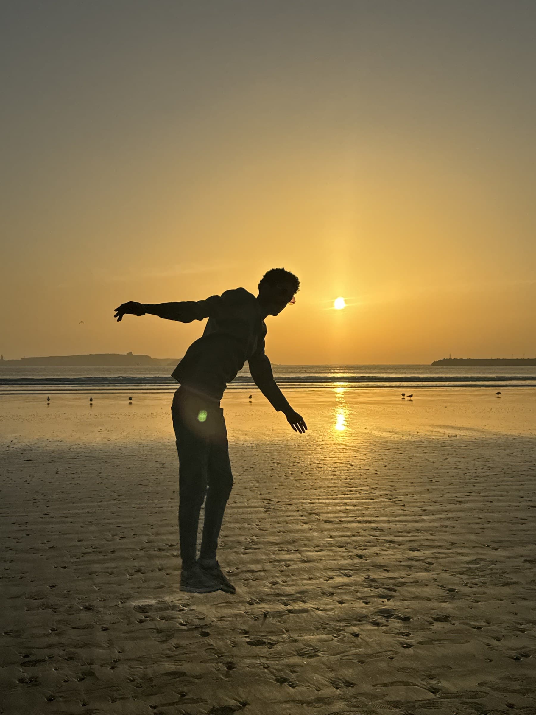 Silueta de persona en playa atlántica de Marruecos al atardecer con cielo dorado y sol en el horizonte
