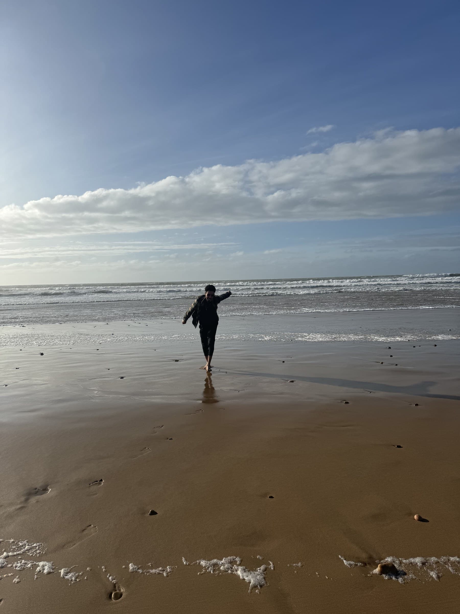 Persona caminando descalza por la playa atlántica de Marruecos con olas y cielo azul al fondo