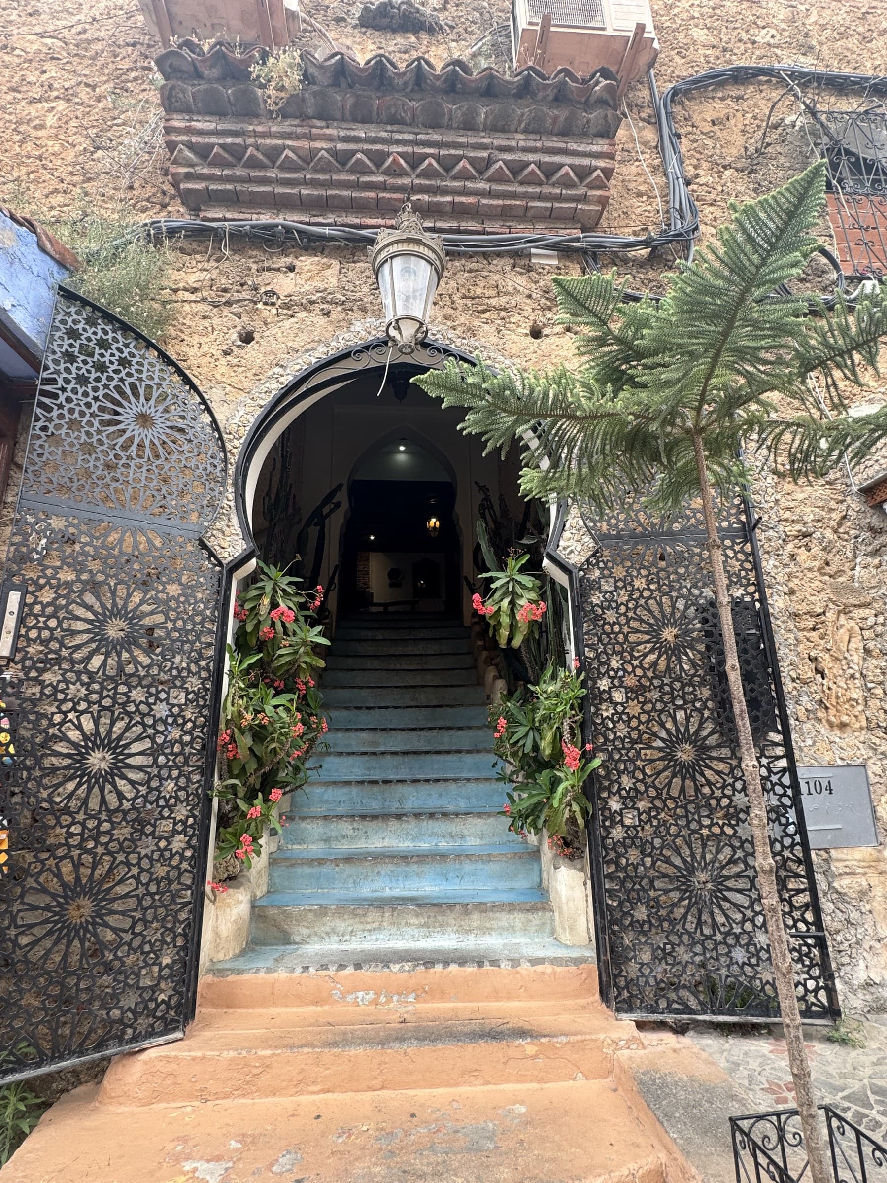 Entrada árabe con arco de herradura, puertas de forja calada y escaleras azules con flores en la medina de Tánger