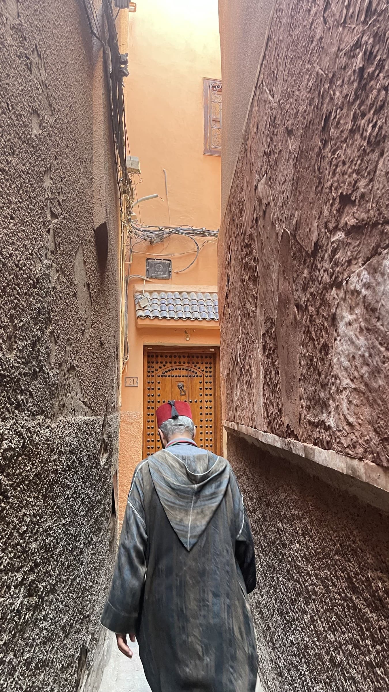 Hombre con djellaba y fez caminando por callejón estrecho de la medina de Fez, Marruecos