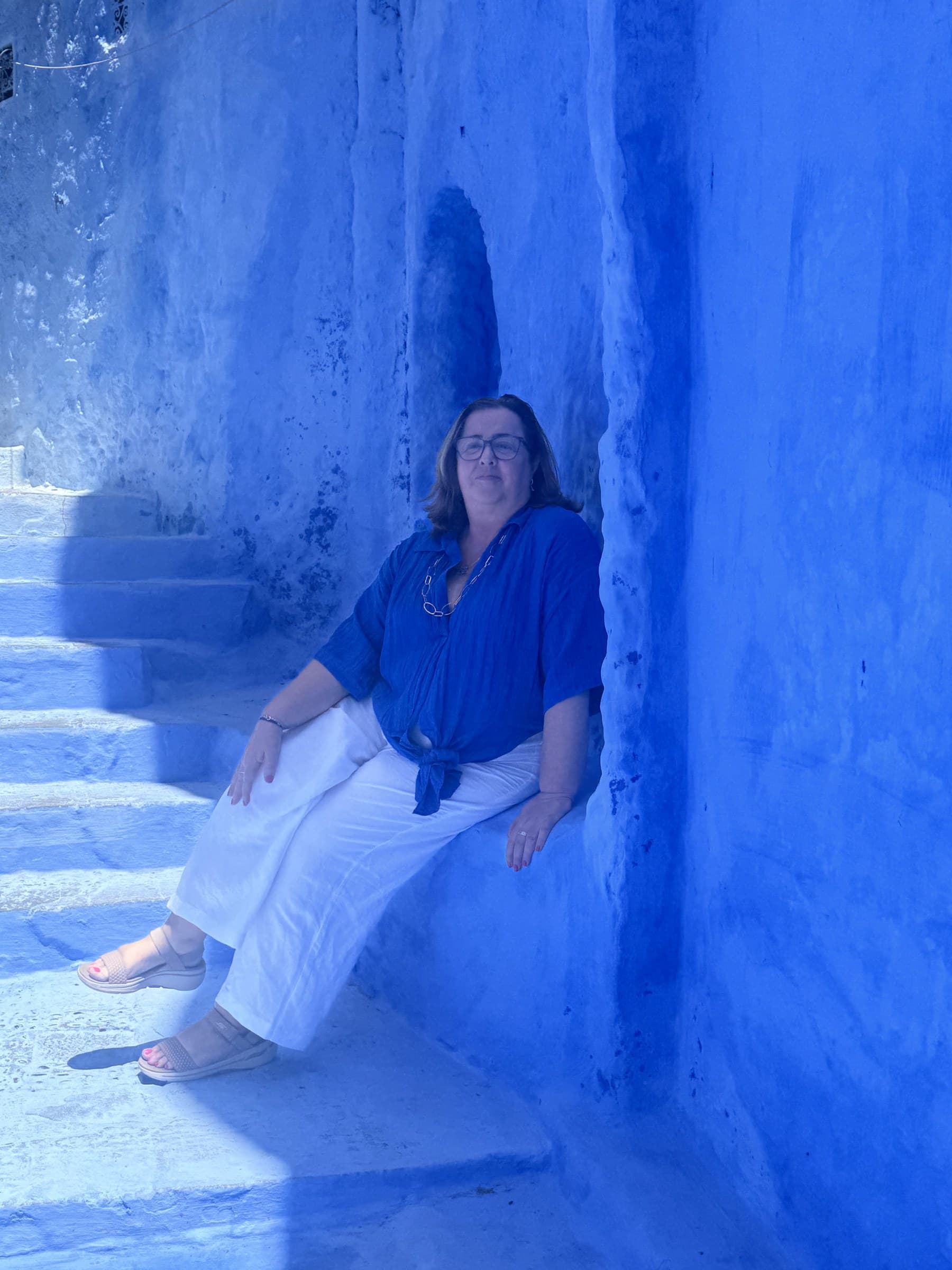 Turista sentada en escaleras azules de la medina de Chefchaouen, la ciudad azul de Marruecos