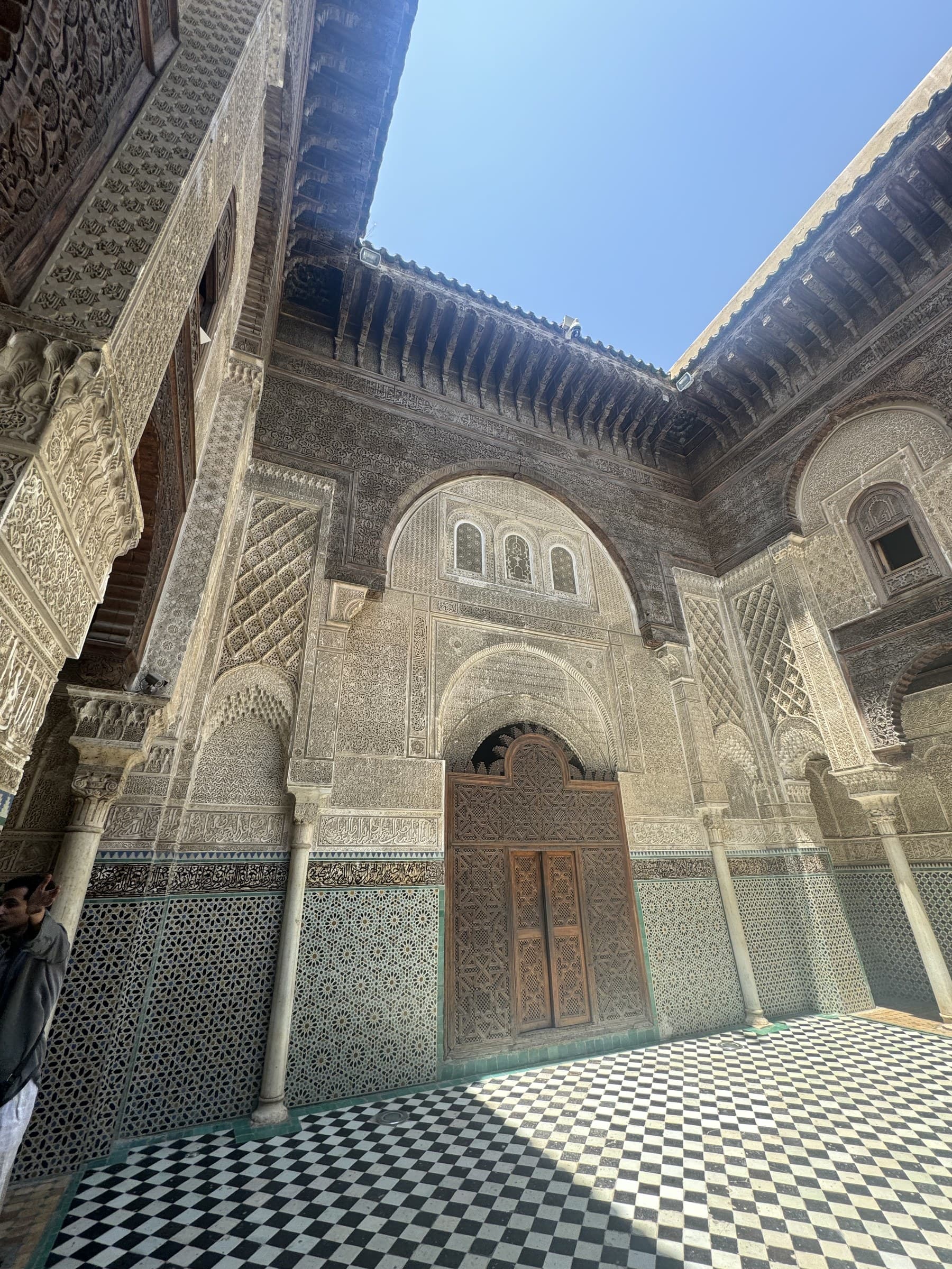 Patio interior de la madrasa Bou Inania de Fez con arcos de yeso tallado, zellij y puerta de madera