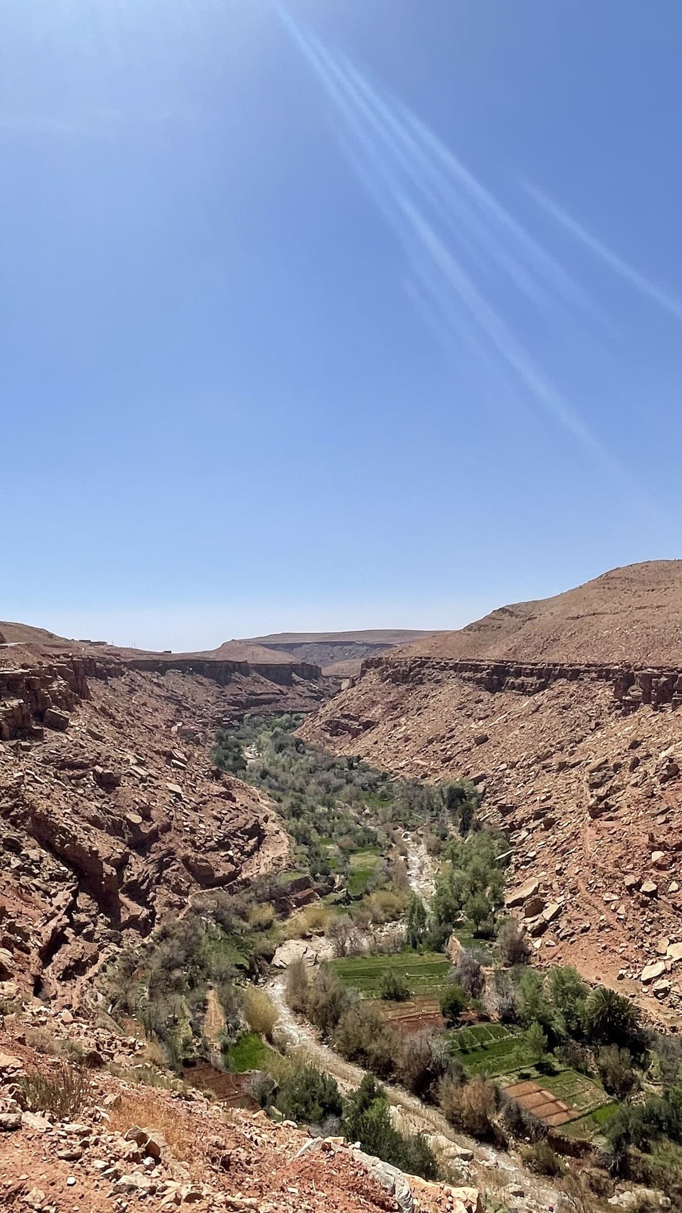 Valle del Dadés desde las alturas con oasis verde entre paredes rocosas rojizas y cielo azul, Marruecos