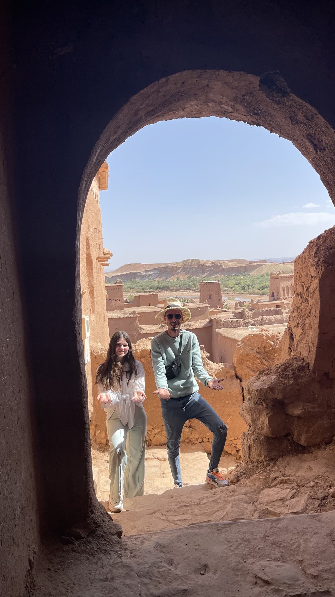 Turistas posando en arco de barro de Aït Ben Haddou con panorámica de la kasbah UNESCO al fondo, Marruecos
