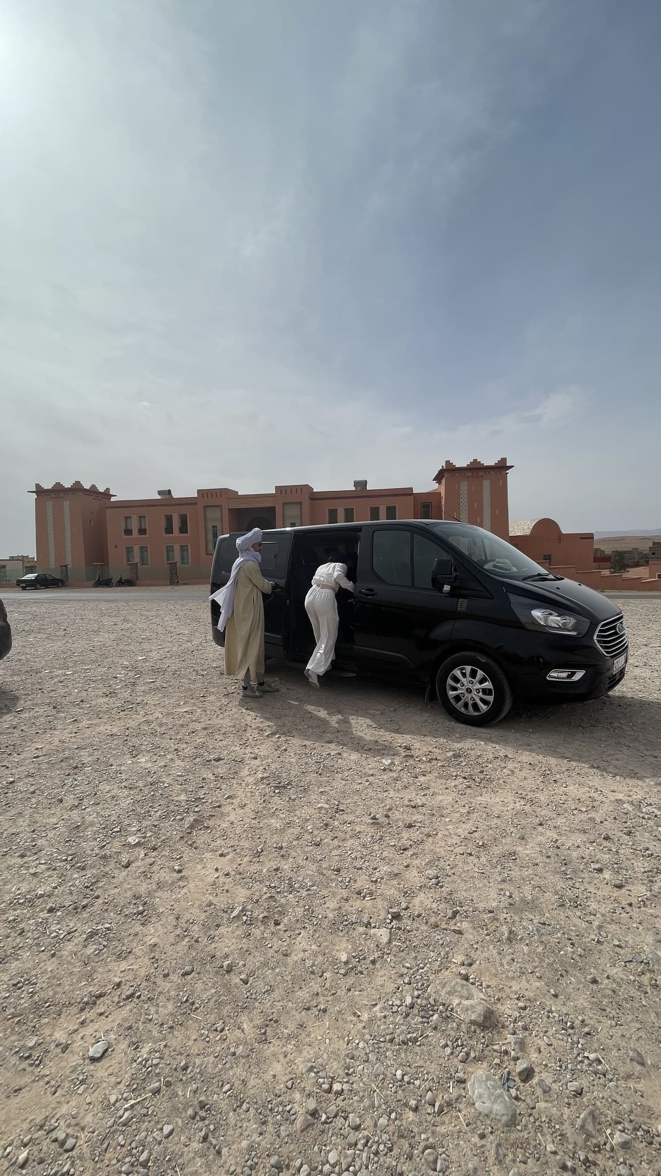 Guías bereberes con túnica blanca subiendo a furgoneta privada negra en el desierto de Merzouga, Marruecos