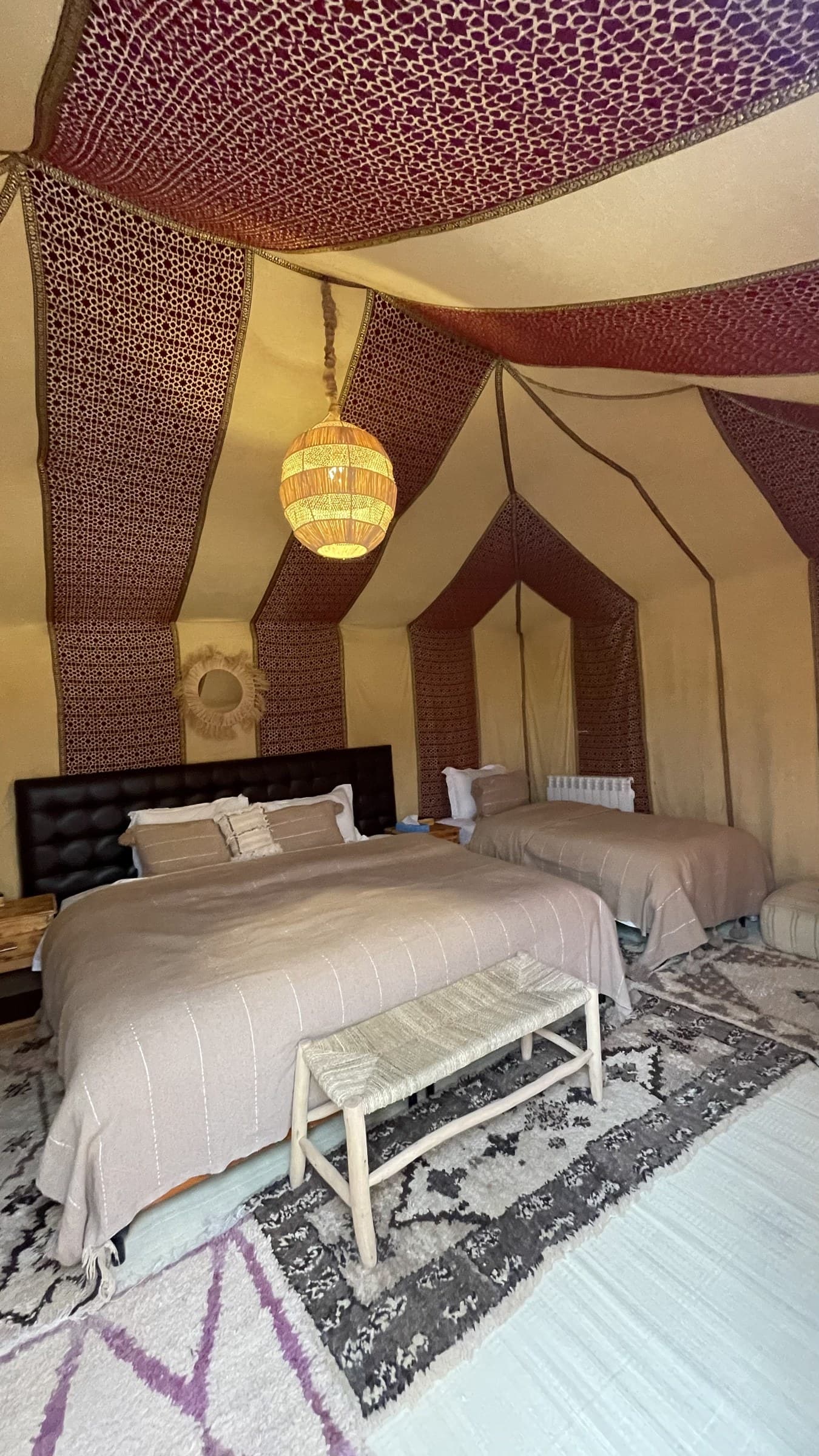 Interior de jaima de lujo en el desierto de Merzouga con dos camas, alfombras bereberes y lámpara artesanal