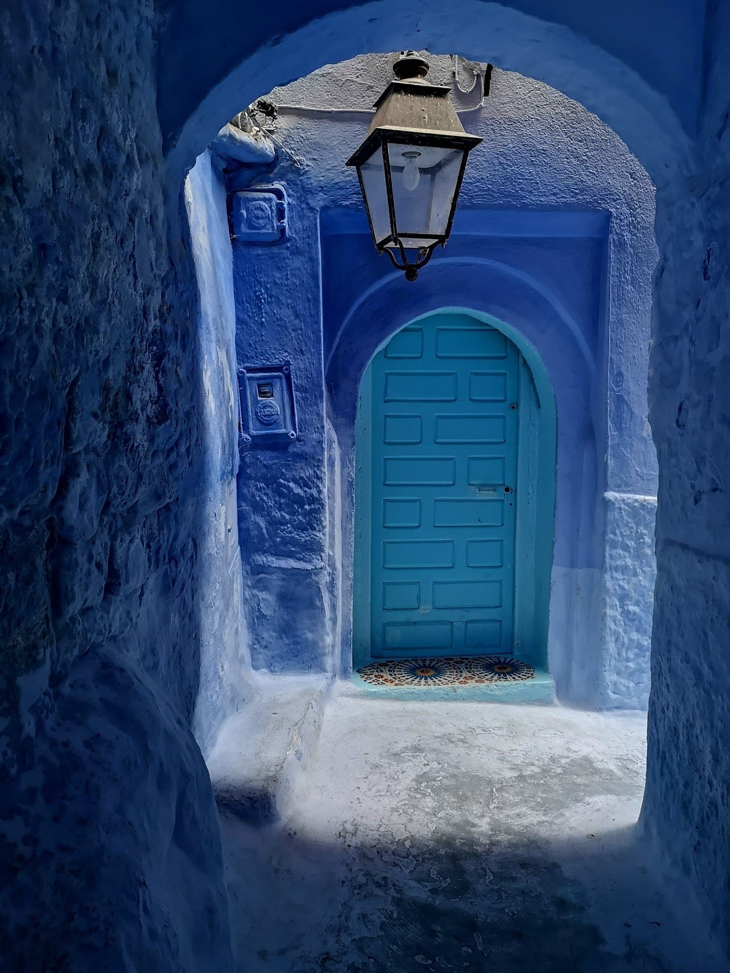 Callejón azul de Chefchaouen con puerta turquesa arqueada y farol de hierro forjado en la medina