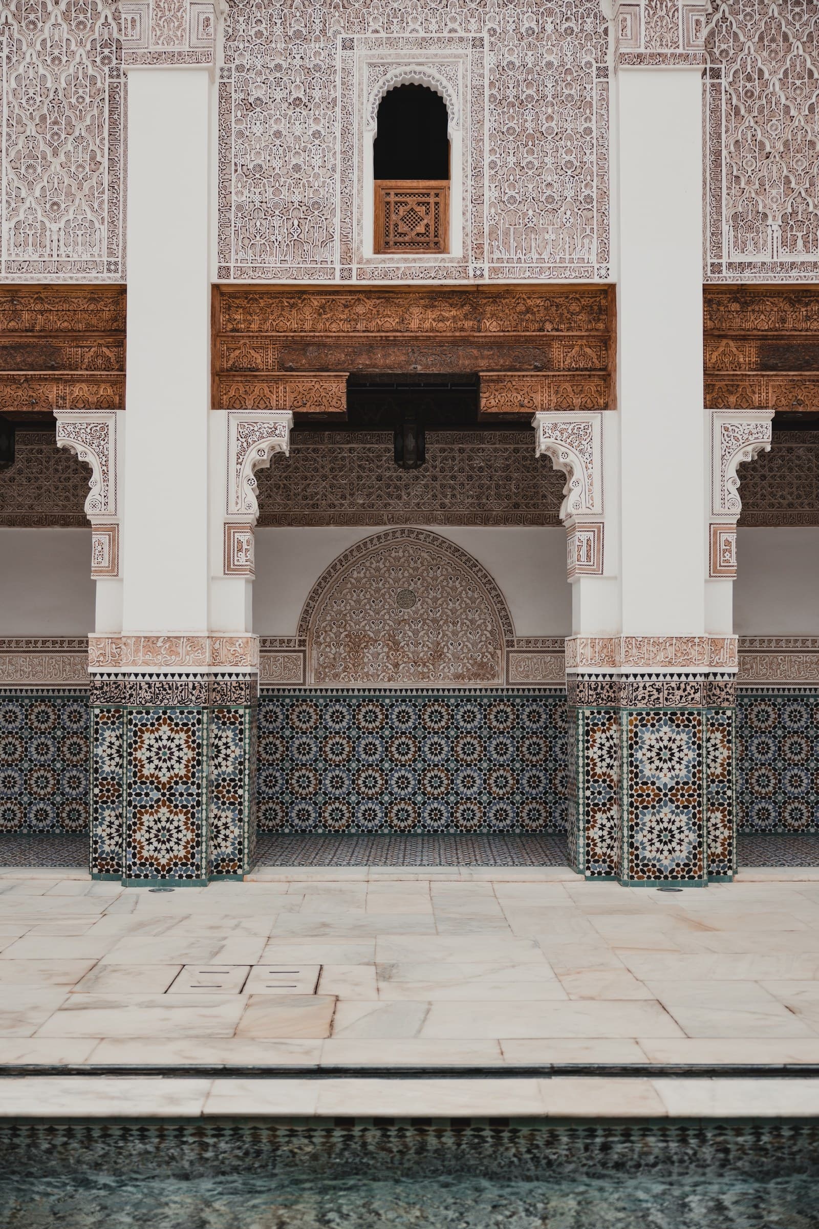 Patio interior de madrasa marroquí con zócalo de mosaicos zellige, arcos de yeso tallado y estanque reflectante
