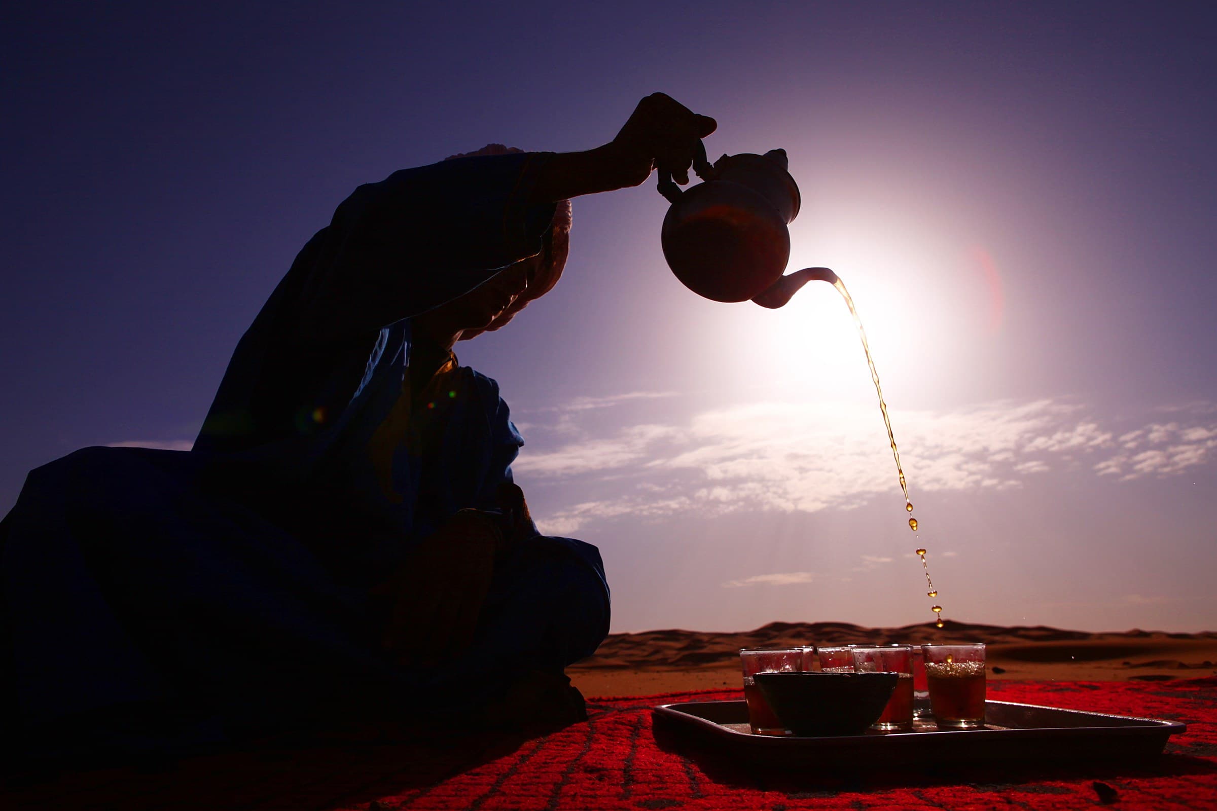 Silueta de nómada bereber sirviendo té moruno en el desierto del Sahara al atardecer, Merzouga