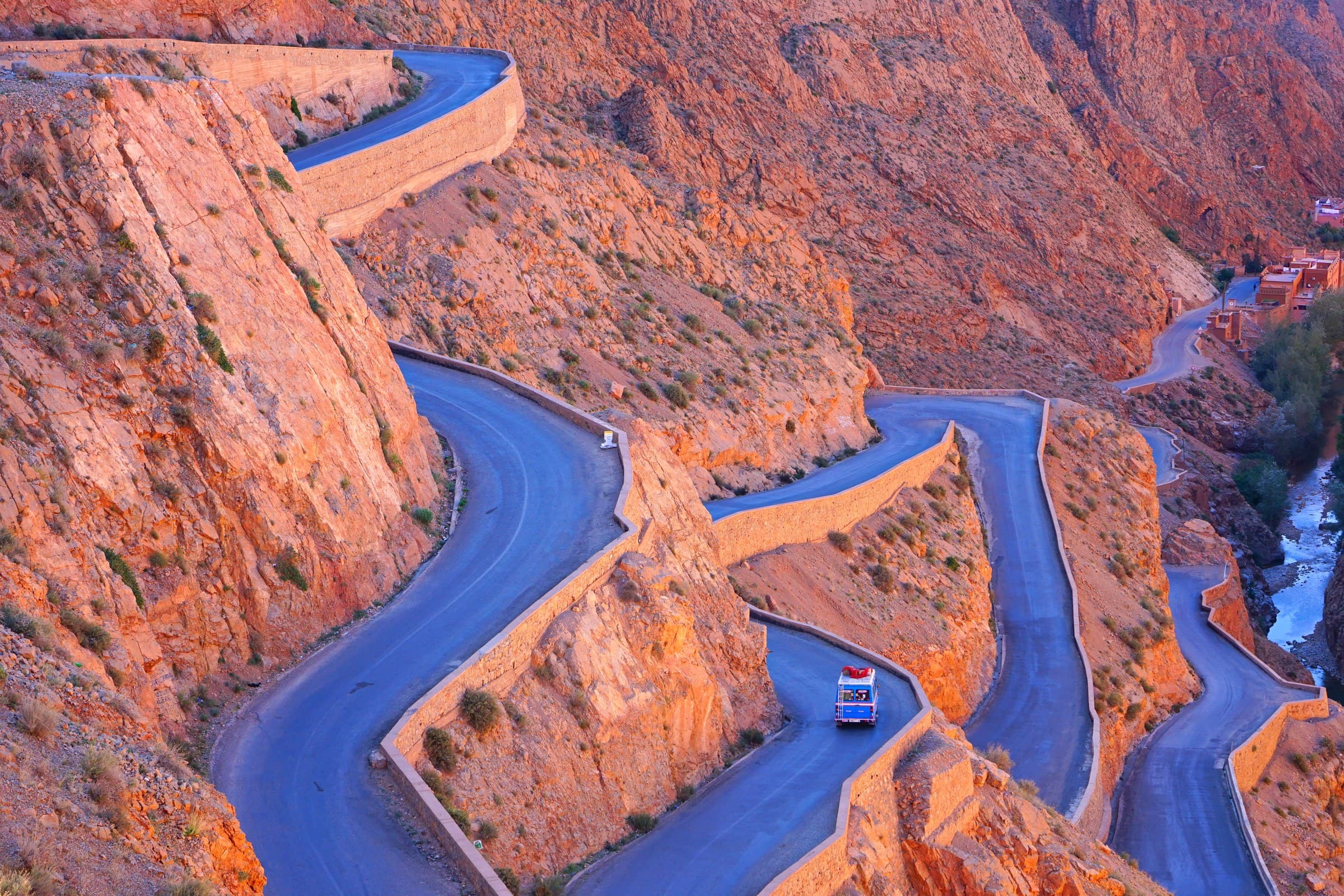 Carretera serpenteante entre las gargantas del Dadés con paredes rocosas rojizas y un autobús azul en Marruecos
