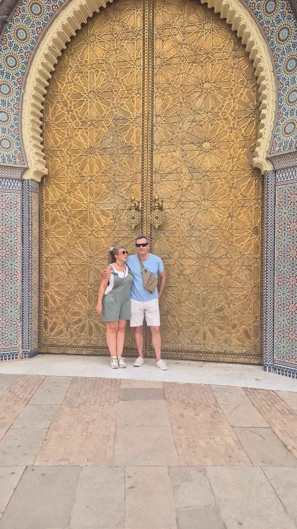 Pareja de viajeros frente a las puertas doradas del Palacio Real de Fez con mosaicos de zellige