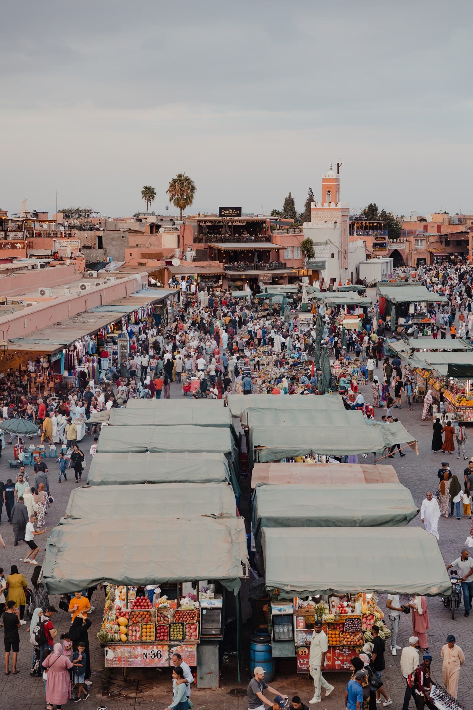 Vista aérea de la plaza Jemaa el-Fna de Marrakech con puestos de frutas, multitudes y minarete al fondo