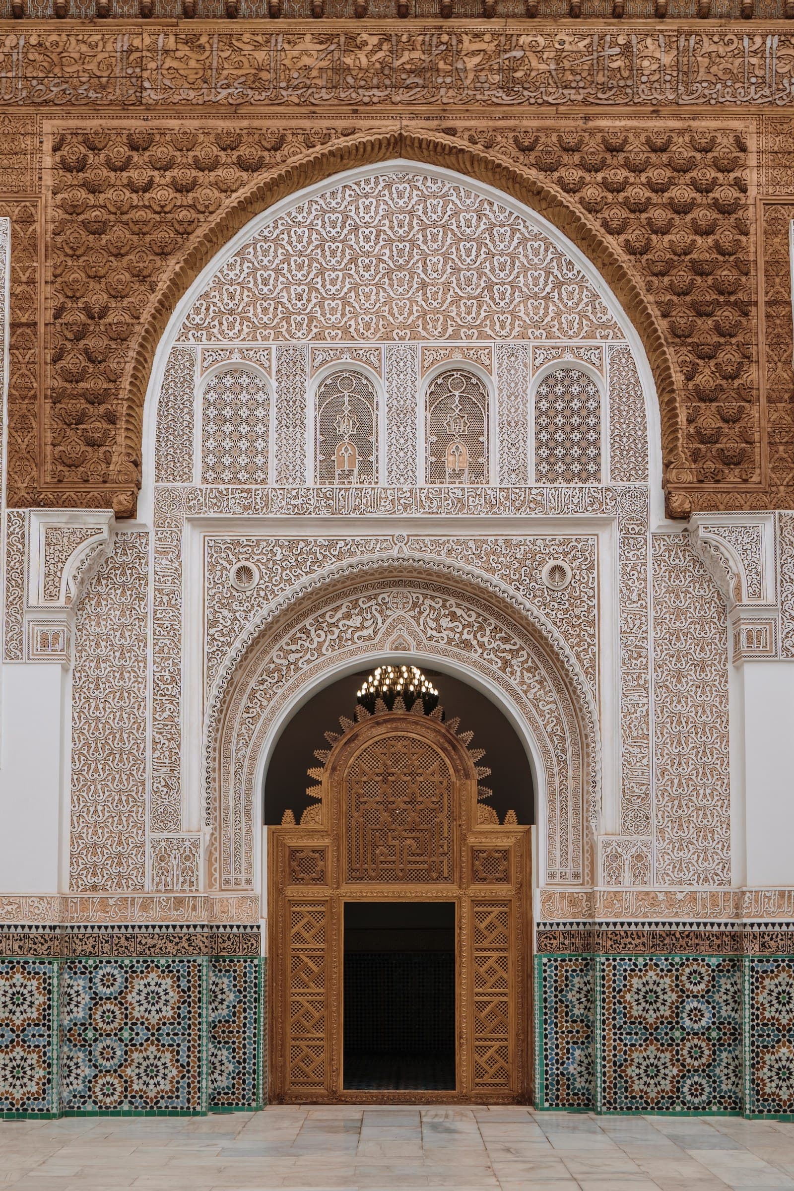 Madrasa Ben Youssef de Marrakech: arco de yesería tallada, puerta dorada y zócalo de mosaico tradicional marroquí