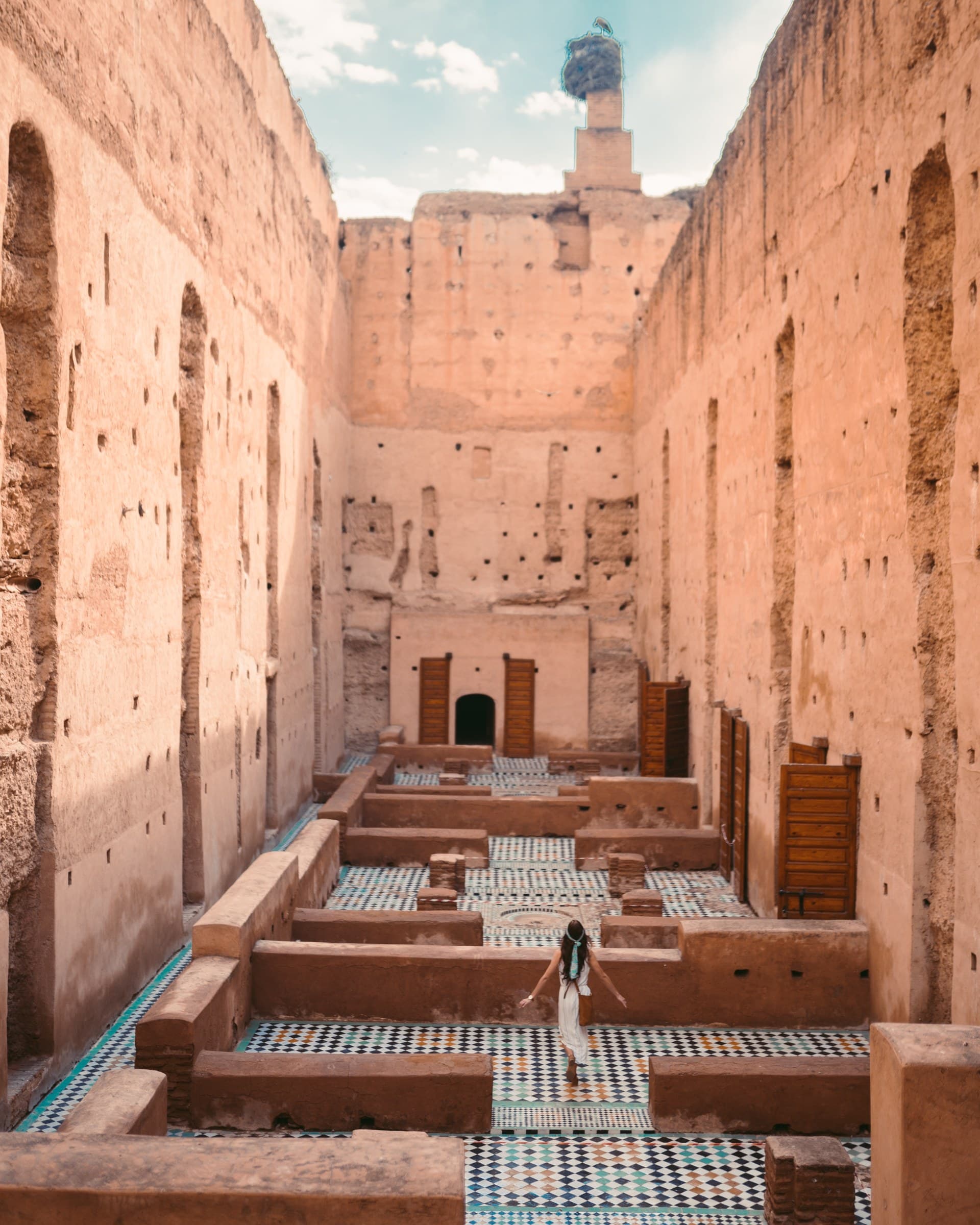 Viajera explorando las ruinas del Palacio El Badi de Marrakech con suelos de mosaico y cigüeña en lo alto